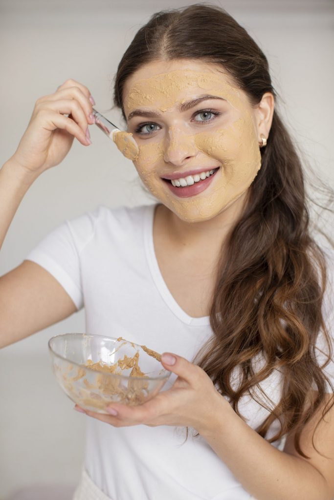 فتاة تمسك بوعاء يحتوي على ماسك من الخميرة وتقوم بتطبيقة على وجهها