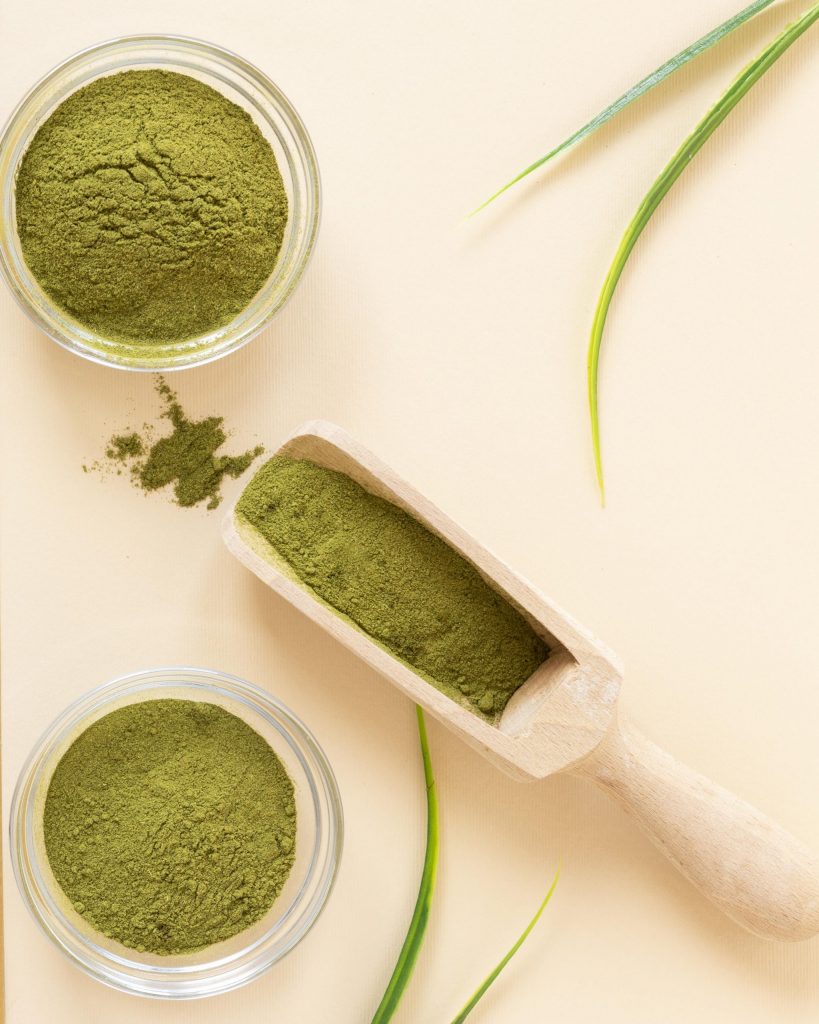 وعاءين من بودرة الحنة وملعقة خشبية مليئة أيضاً بالبودرة وعروق خضراء